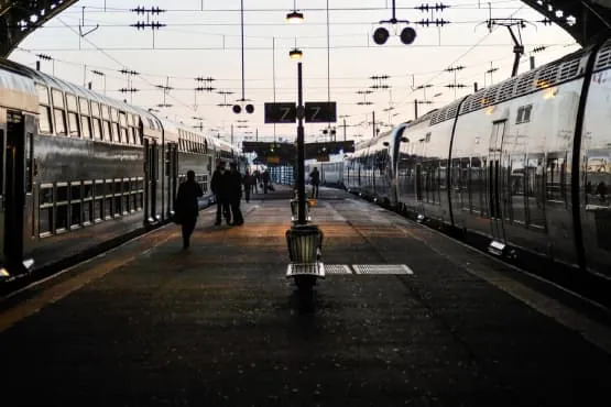 vtc gare toulouse Matabiau Passants sur une voie piétonne devant une gare en soirée.