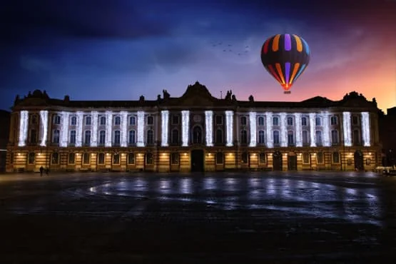 cité de l'espace à Toulouse Façade d’un bâtiment éclairé la nuit, avec son reflet sur le sol mouillé.